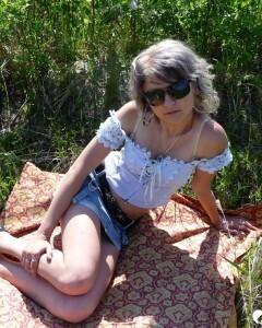 Gray-haired beauty posing naked outdoors on a blanket