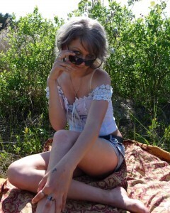 Gray-haired beauty posing naked outdoors on a blanket