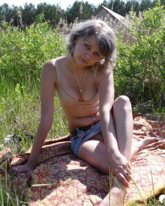 Gray-haired beauty posing naked outdoors on a blanket